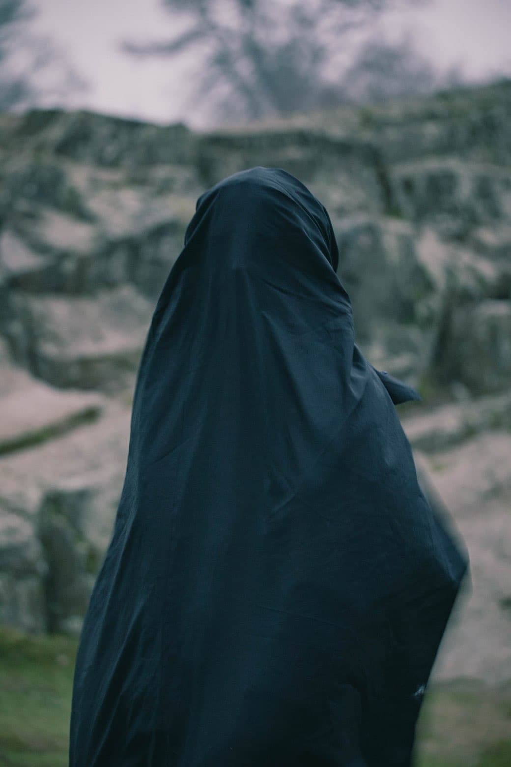 Figure draped in dark fabric in a mountain landscape