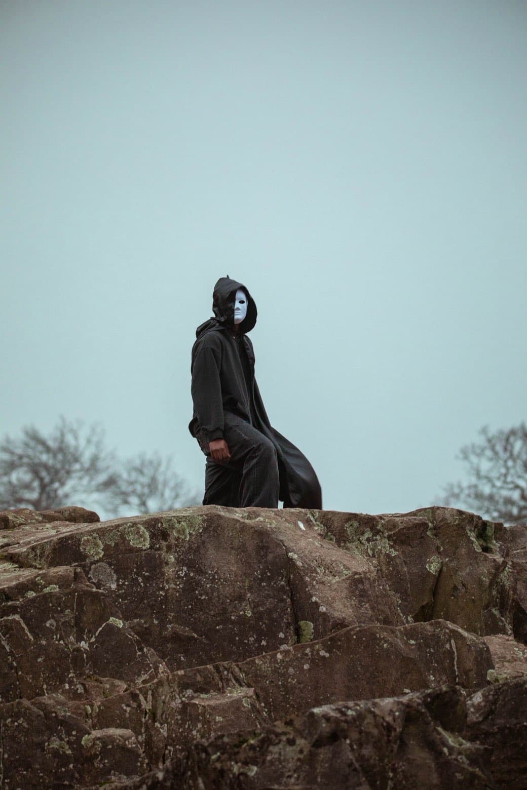 Veiled figure seated on rocks in an open landscape
