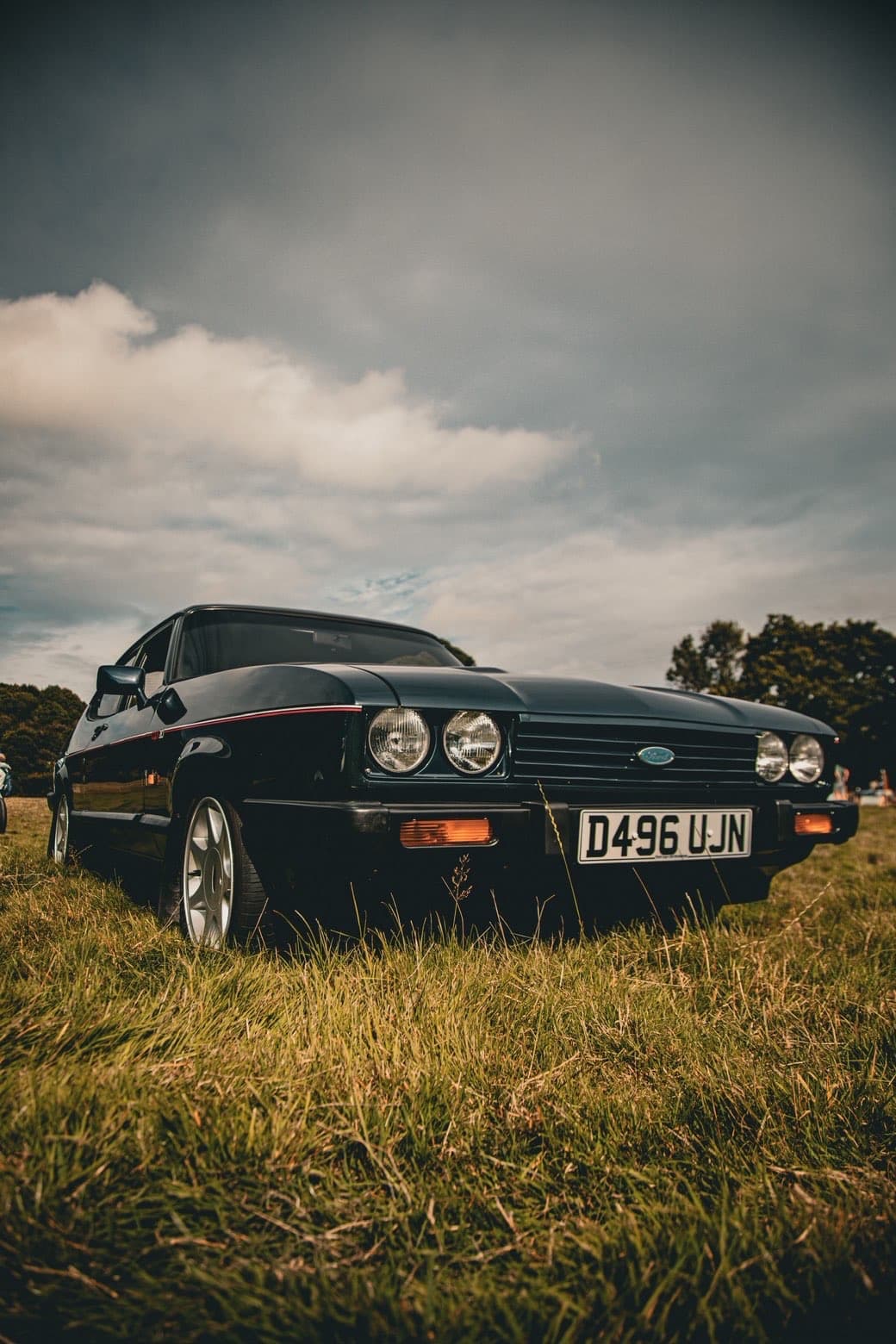 Vintage car photographed in a grassy field under dramatic clouds